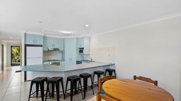 Una cocina moderna con una isla central, taburetes de bar, una mesa de comedor de madera y vistas a un jardín.