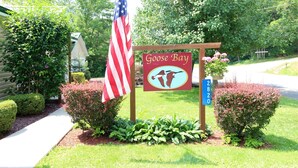 A sign for Goose Bay with an American flag, a number sign, and a logo. - Cooperstown Baseball Rentals - Goose Bay (Portlandville)