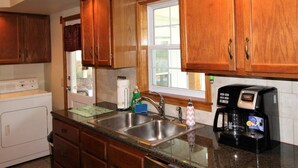 A kitchen with wooden cabinets, a stainless steel sink, a coffee maker, and a window with a view. - Cooperstown Baseball Rentals - Goose Bay (Portlandville)