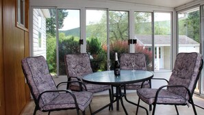A conservatory with a round table and four chairs, large windows, and a bottle of champagne. - Cooperstown Baseball Rentals - Goose Bay (Portlandville)