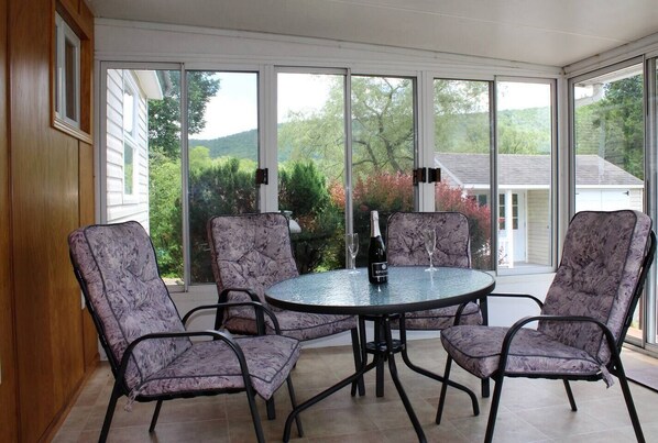 A conservatory with a round table and four chairs, large windows, and a bottle of champagne. - Cooperstown Baseball Rentals - Goose Bay (Portlandville)