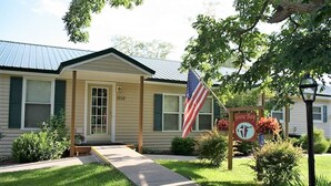 A single-story house with a front porch, a flag, and a sign indicating it is a Goose Bay establishment. - Cooperstown Baseball Rentals - Goose Bay (Portlandville)