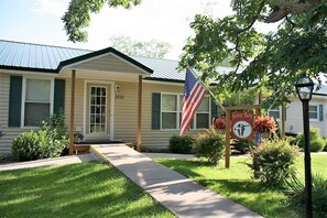 A single-story house with a front porch, a flag, and a sign indicating it is a Goose Bay establishment. - Cooperstown Baseball Rentals - Goose Bay (Portlandville)