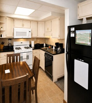A kitchen with white cabinets, a black refrigerator, a stove, and a dining table with chairs. - Cooperstown Baseball Rentals - 2nd Baseman (Oneonta)