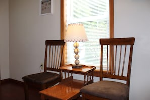 A room with two wooden chairs and a small table, a lamp on the table, and a window with blinds.