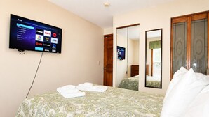 Habitació d'hotel amb llit, televisió penjada a la pared que mostra canals, mirall i armari.
