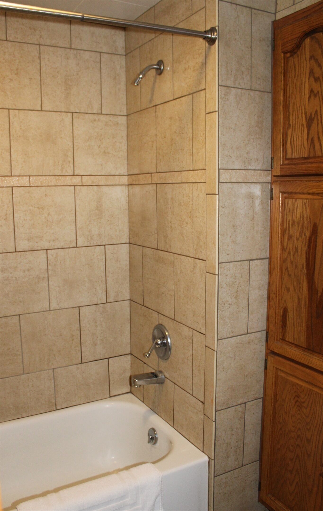 A bathroom with beige tiled walls, a white bathtub, and wooden cabinetry.