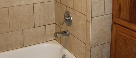 A bathroom with beige tiled walls, a white bathtub, and wooden cabinetry.
