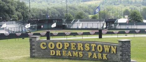 A sign for Cooperstown Dreams Park with a stone base and a grassy field in the background.