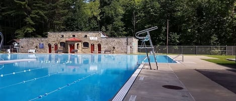 A swimming pool with lane dividers, a lifeguard chair, and a stone building with red doors in the background.