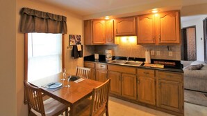 Una cocina compacta con armarios de madera, una mesa de comedor con sillas y un ventanal con cortinas.