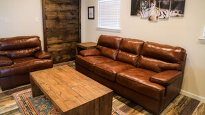 Un salon avec un canapé en cuir marron, une table basse en bois et un tapis à motifs.