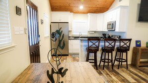 Une cuisine avec des meubles blancs, un plafond en bois et un coin repas comprenant une table et des chaises en bois.