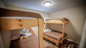Une chambre avec deux lits superposés, des têtes de lit en bois et un luminaire au plafond.