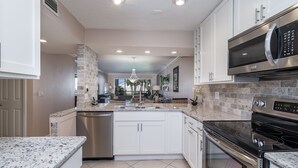 A modern kitchen with white cabinets, granite countertops, stainless steel appliances, and a central island. - Little slice of paradise, Siesta Dunes 2-209. (Siesta Key)