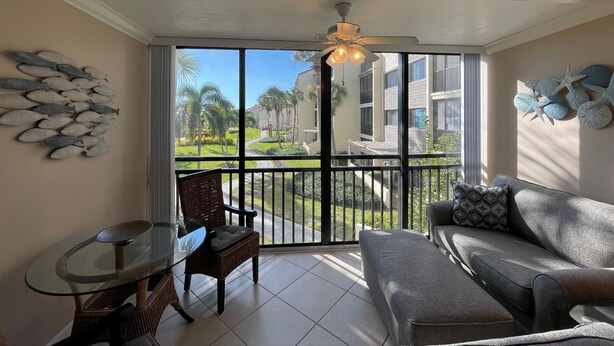 A room with a glass door leading to a balcony, a sofa, a chair, and a small table. - Little slice of paradise, Siesta Dunes 2-209. (Siesta Key)