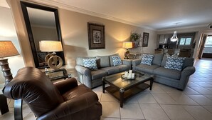 A living room with a brown leather sofa, a grey sofa with patterned cushions, a glass coffee table, and a large mirror. - Little slice of paradise, Siesta Dunes 2-209. (Siesta Key)