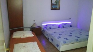 A small, single-bed room with a wooden headboard, a bedside table, and a nightstand. There is a painting on the wall above the bed.