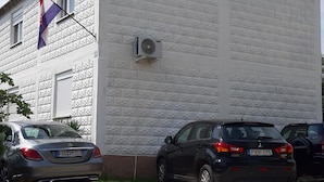 A building with a white exterior and a flag. There are two cars parked in front.