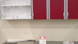 A kitchenette with red cabinets, a stainless steel sink, and a white countertop.