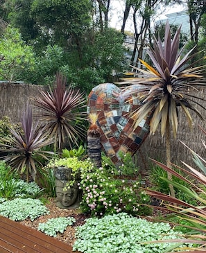 Un jardín con una escultura de piedra, diversas plantas y una valla de madera.