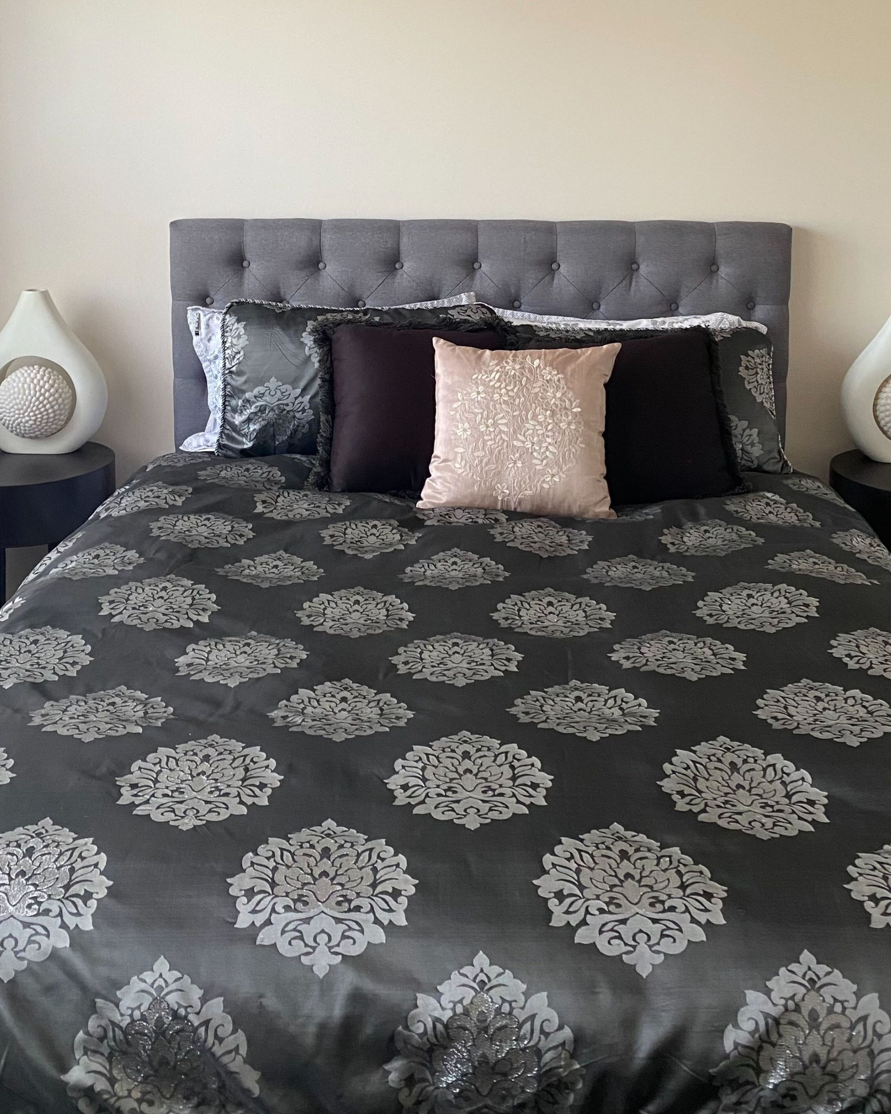 A bed with a tufted headboard, a patterned bedspread, and two bedside tables with lamps.