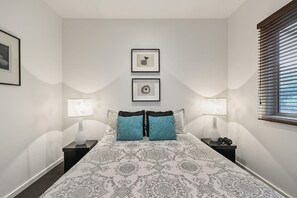 Un dormitorio con una colcha estampada, dos almohadas, dos lámparas de noche y dos cuadros en la pared.