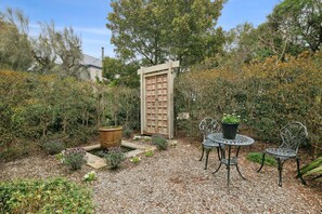 Un jardín con una reja de madera, una mesa de metal con sillas y diversas plantas.