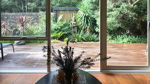 A view through a glass door into a garden with a wooden deck, a statue, and various plants.