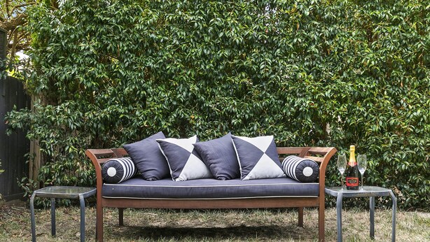 A wooden outdoor sofa with cushions, two metal tables, and a bottle of champagne. - Aireys Oasis (Aireys Inlet)