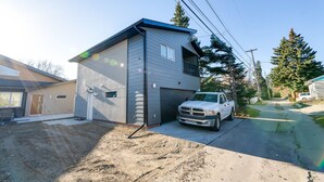 Een gebouw met twee verdiepingen, een garage, en een witte pick-up truck die ervoor geparkeerd staat, met een onverharde oprit.