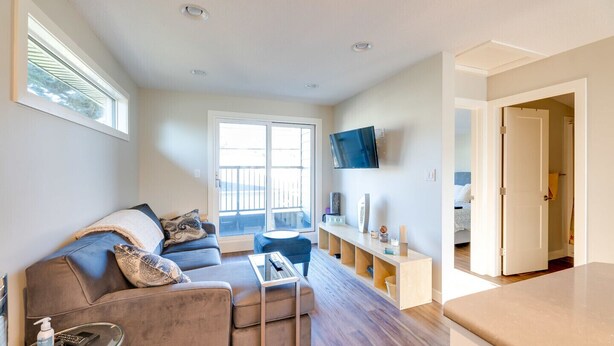Een moderne woonkamer met een grijze bank, een glazen salontafel en een aan de muur bevestigde televisie.