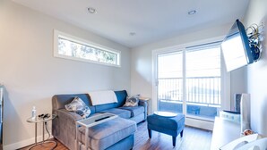 Een moderne woonkamer met een blauwe bank, een klein rond tafeltje en een groot raam met uitzicht op de omgeving.