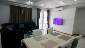 Ein modernes Wohnzimmer mit einer Couch, einem Esstisch mit Stühlen, einem flachbildfernseher an der Wand und einer Klimaanlage.