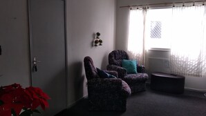 A room with two patterned armchairs, a small ottoman, a door, and a window with sheer curtains. - Apartment on Estrada do Pré in Campo Grande (Sen. Vasconcelos)