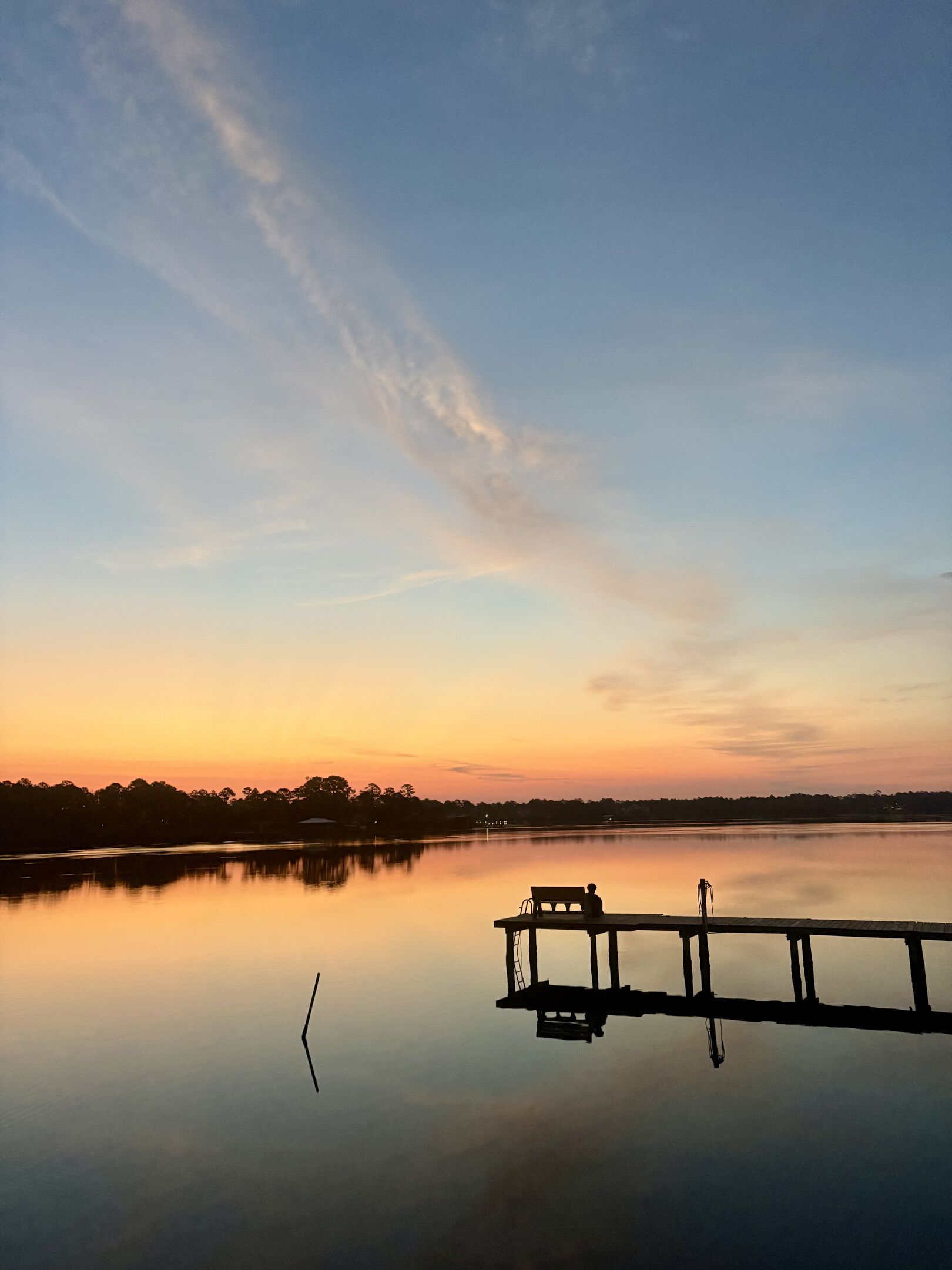 A calm lake at sunset with a dock and a bench.