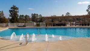 Una piscina con chorros de agua, una zona de estar techada y una terraza cercada.