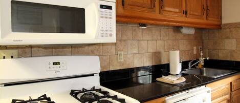 A kitchen with a white stove, a microwave, wooden cabinets, a black countertop, and a dishwasher.
