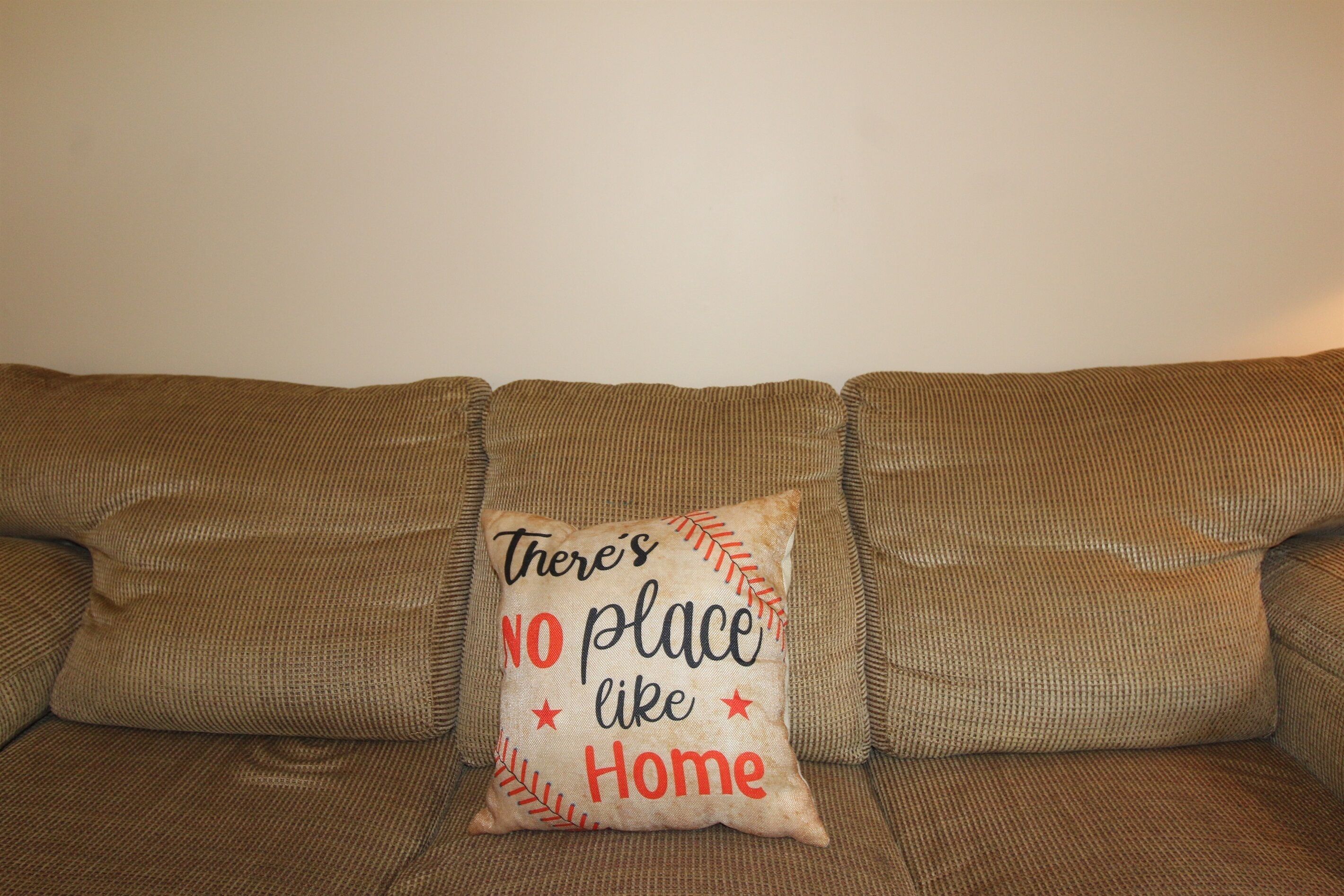 A brown couch with a pillow that reads "There's no place like Home."