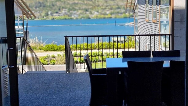 Un balcone con tavolo e sedie, vista su un lago e delle colline.