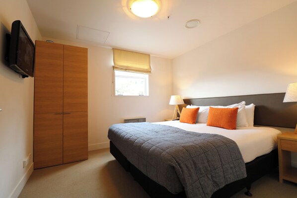 A bedroom with a bed, bedside lamps, a TV, and a wardrobe.