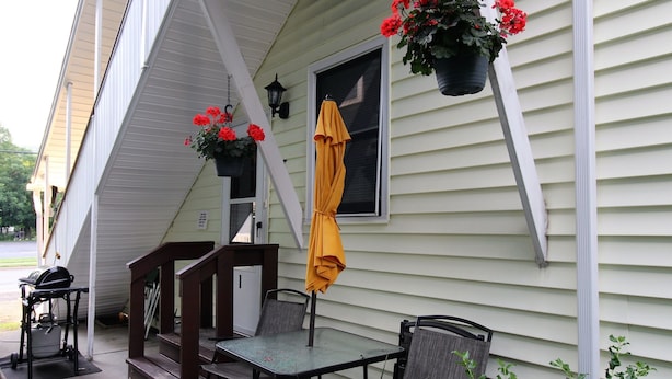 A patio with a table and chairs, a yellow umbrella, and hanging flower baskets. - Cooperstown Baseball Rentals - Championship #1 (Oneonta)