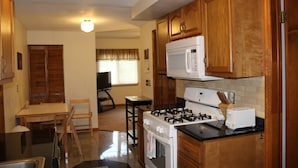 A compact kitchen with wooden cabinets, a gas stove, a microwave, and a toaster. - Cooperstown Baseball Rentals - Championship #1 (Oneonta)