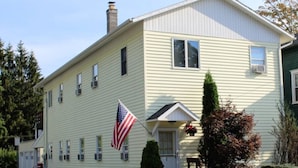A two-story house with a front porch, a chimney, and an American flag. - Cooperstown Baseball Rentals - Championship #1 (Oneonta)