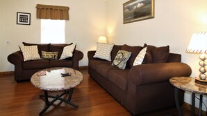 A living room with two brown sofas, a round coffee table, a lamp, and a framed picture on the wall. - Cooperstown Baseball Rentals - Championship #1 (Oneonta)