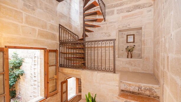 Eine Wendeltreppe mit schmiedeeisernem Geländer, einer Zimmerpflanze und einem kleinen gerahmten Bild an der Wand.