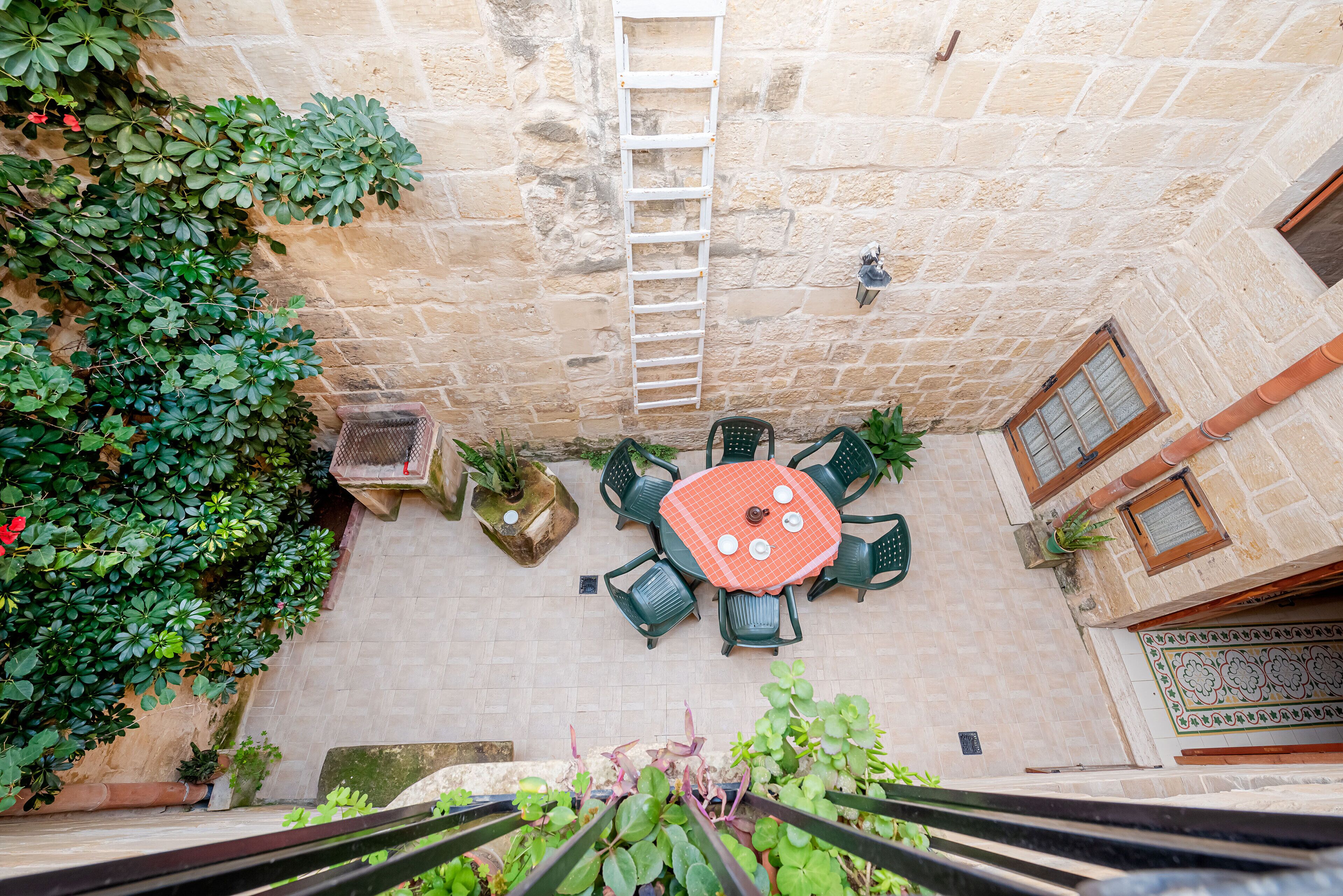 A courtyard with a table and chairs, surrounded by plants and a stone wall.