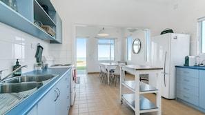 A modern kitchen with a view of the beach, a dining area, and a refrigerator.
