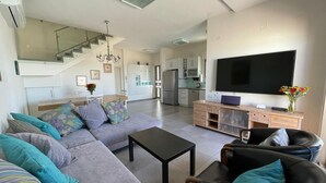 Un salon moderne avec un canapé, une table basse et un téléviseur. Un escalier mène à un niveau supérieur.