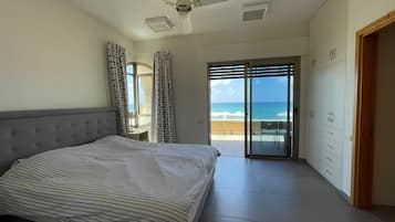 A bedroom with a bed, a ceiling fan, a view of the ocean through a sliding door, and a wardrobe.
